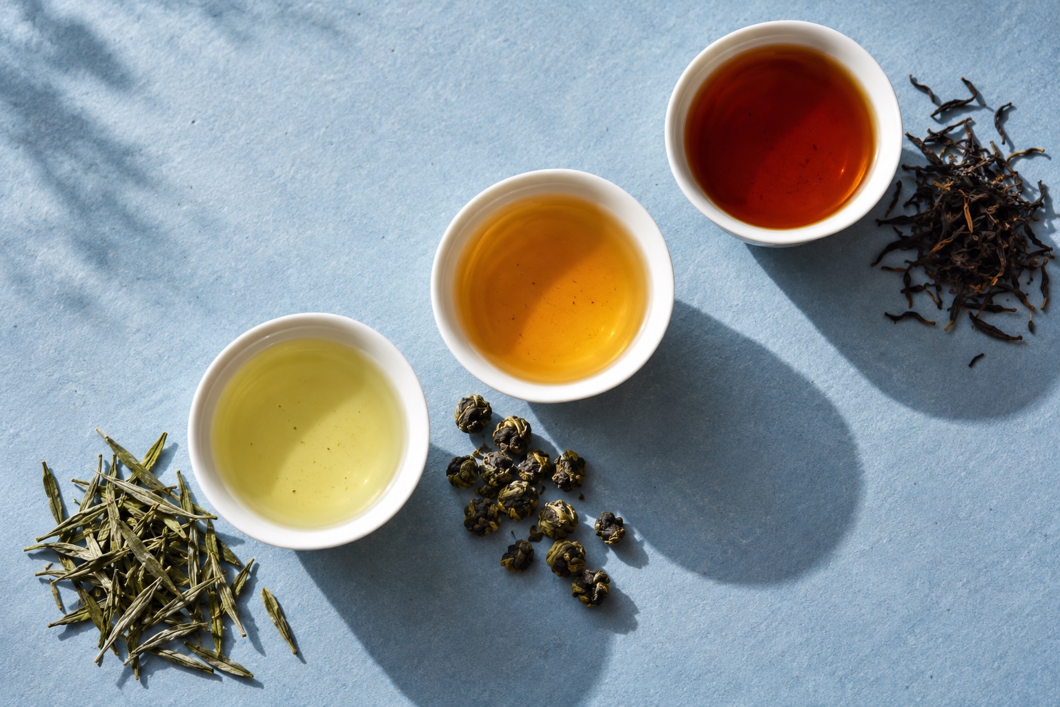 Three different tea infusions and loose leaves on a pale blue surface